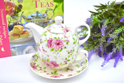 Decorative teapot with floral pattern on a saucer, next to a book titled 'Seasonal Recipes' and purple flowers.