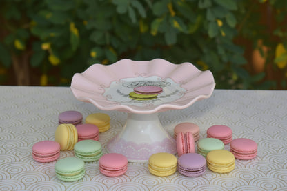 Decorative pink and white ceramic cake stand with a scalloped edge on a patterned surface.