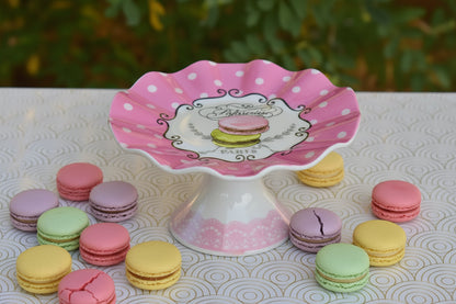 Pink polka dot cake stand with a decorative emblem on a patterned surface.