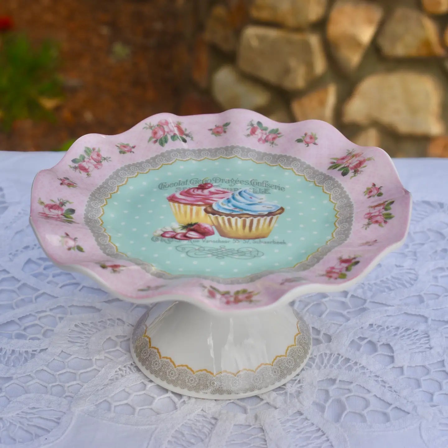 Decorative cake stand with floral design and cupcake illustration on a lace tablecloth.