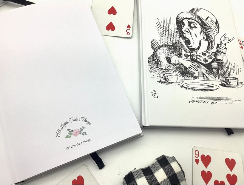 Notebook with Alice in Wonderland illustration and playing cards on a white surface